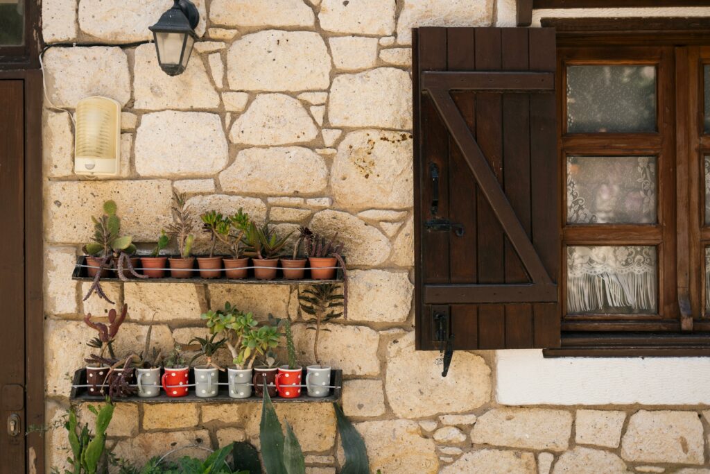 Charming rustic stone wall with potted succulents and a wooden shuttered window.