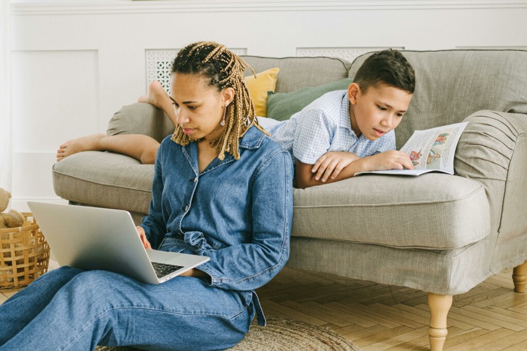 A mother and son enjoying leisure activities indoors with a laptop and book.